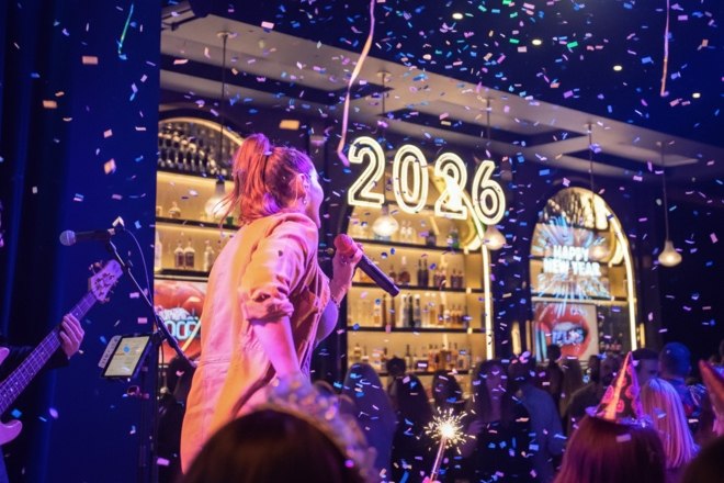 A live band performs on New Year’s Eve as confetti falls and a glowing “2026” sign lights up the celebration.
