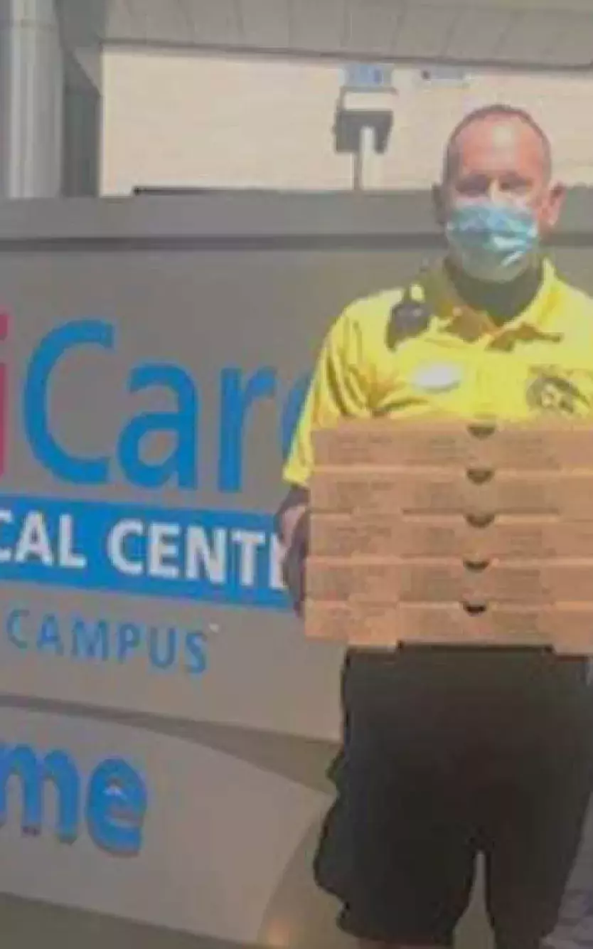 Man holding boxes of pizza stands in front of the sign for a medical facility